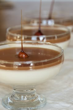 three desserts are sitting in small glass bowls on a white tablecloth, one is drizzled with caramel