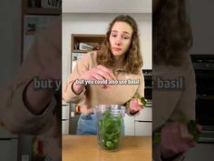 a woman standing in front of a counter with a jar filled with green liquid and vegetables