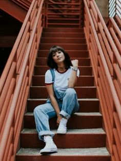 a woman sitting on some stairs with her hand in her pocket and looking up at the camera