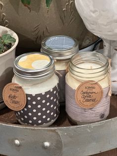 three jars filled with candles sitting on top of a wooden table next to a potted plant