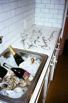 two bottles of champagne sitting in an ice bucket on top of a sink filled with oysters