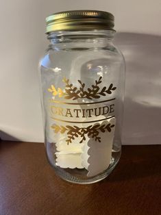 a glass jar filled with white paper and gold lettering on top of a wooden table