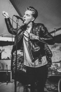 a man singing into a microphone while standing in front of a stage with other musicians