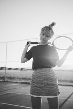 a woman holding a tennis racquet on top of a tennis court with the sun behind her