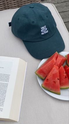 watermelon slices are on a plate next to a book and cap sitting on a table