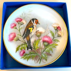 a plate with a bird painted on it in a blue box next to pink flowers