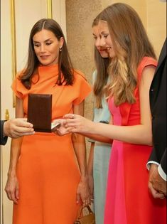 two women in orange dresses looking at a chocolate box