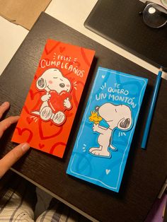 two notebooks with cartoon characters on them sitting on a table next to a person's hand