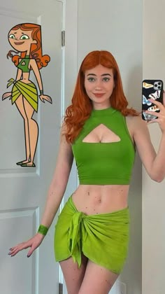 a woman with red hair and green outfit holding up a cell phone