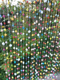 a multicolored mobile hanging in front of a green bush with flowers on it