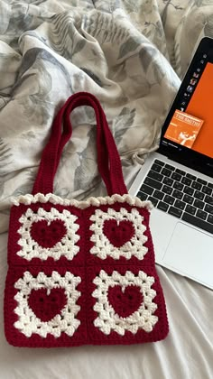 a laptop computer sitting on top of a bed next to a crocheted bag