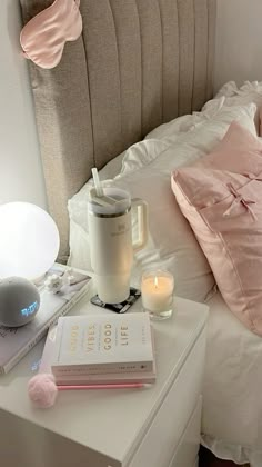 a bed with pink pillows and books on top of it next to a night stand