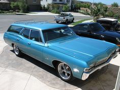 an old blue station wagon is parked in a parking lot with other cars behind it