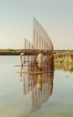 three people are standing in the water near a large bird cage that is shaped like a boat