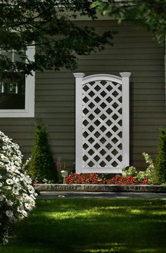 a white trellis on the side of a house with flowers in front of it