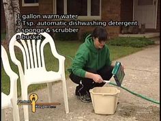 a young man is using a hose to clean a bucket on the sidewalk in front of a house