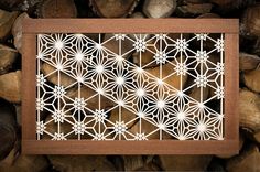 a wooden frame with laser cut designs on it in front of wood logs and firewood