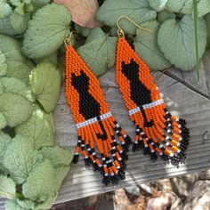 an orange and black beaded earrings on top of a wooden table next to leaves