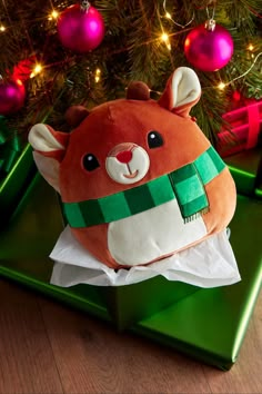 a stuffed animal sitting on top of a green box next to a christmas tree with lights