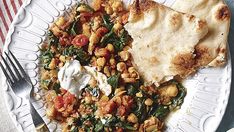 a white plate topped with beans and spinach next to a slice of pita bread