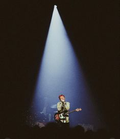 a man standing on top of a stage holding a guitar