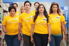 group of people in yellow shirts walking down the aisle with soda cans on shelves behind them