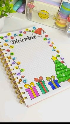 a spiral notebook with christmas decorations and writing on the cover is sitting on a desk next to other office supplies