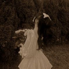 an old photo of a woman in a white dress holding flowers up to her face