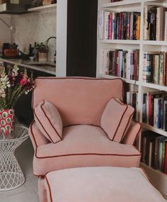 a pink chair and ottoman in front of a bookshelf