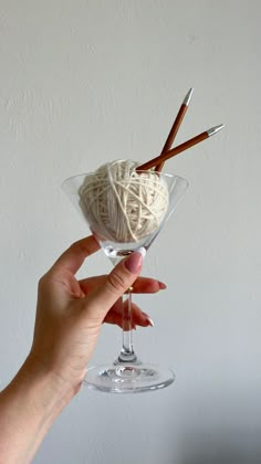 a hand holding a wine glass filled with yarn and two skewers in it