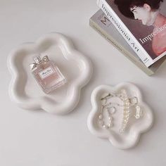 two pieces of white glass sitting on top of a table next to a book and perfume bottle