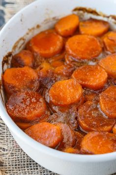 a white bowl filled with cooked carrots sitting on top of a cloth covered table