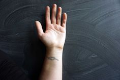 a person's hand with a small tattoo on their left wrist, against a black background