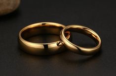 two gold wedding rings sitting next to each other on a black surface with rocks in the background