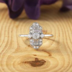 a diamond ring sitting on top of a wooden table with purple flowers in the background