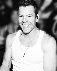 a black and white photo of a smiling man with his eyes closed, wearing a tank top