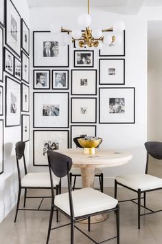 a white dining room with black and white pictures on the wall, two chairs around a round table