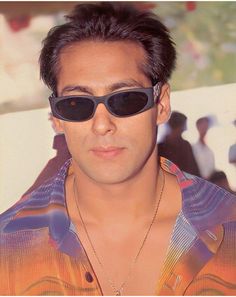 a man with sunglasses on his head wearing a shirt and necklace in front of a wall