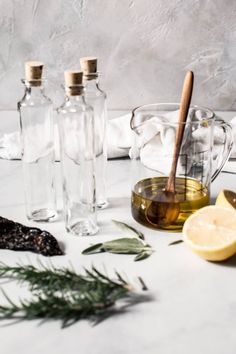 three bottles with olive oil, lemon and rosemary on a white countertop next to other ingredients