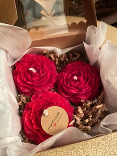 three red flowers in a brown box with paper wrapping around it and a tag on the top