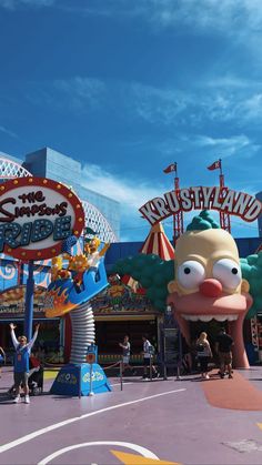 the entrance to an amusement park with people walking around and riding on roller coasters