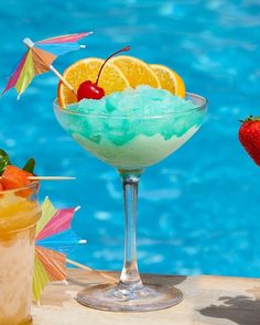 two cocktails with strawberries, orange slices and an umbrella next to a pool