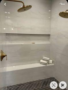 a bathroom with white marble walls and flooring, two gold faucets on the shower head