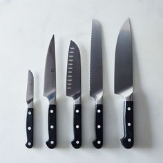 five knives are lined up next to each other on a white counter top with black handles