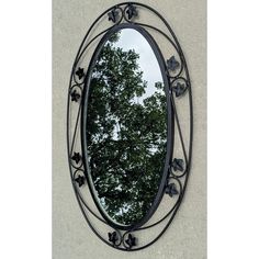 an oval mirror hanging on the side of a wall with trees reflected in it's reflection