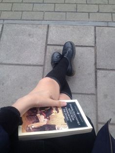 a person sitting on the ground with their feet up and holding a book in front of them