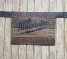 a wooden sign hanging on the side of a building that says millauke with an arrow