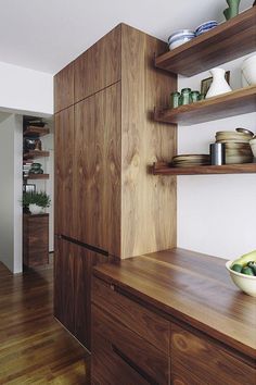 a kitchen with wooden shelves and bowls on the counter top next to a bowl of fruit