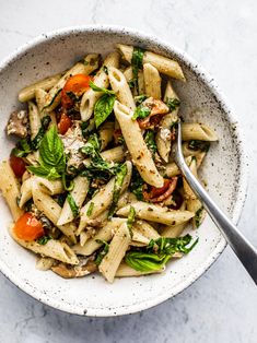 a bowl filled with pasta and vegetables on top of a white countertop next to a fork