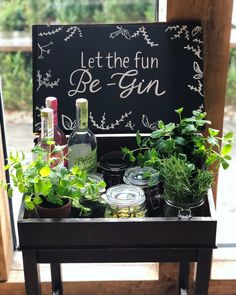 a wooden table topped with potted plants next to a chalkboard that says let the fun be gin